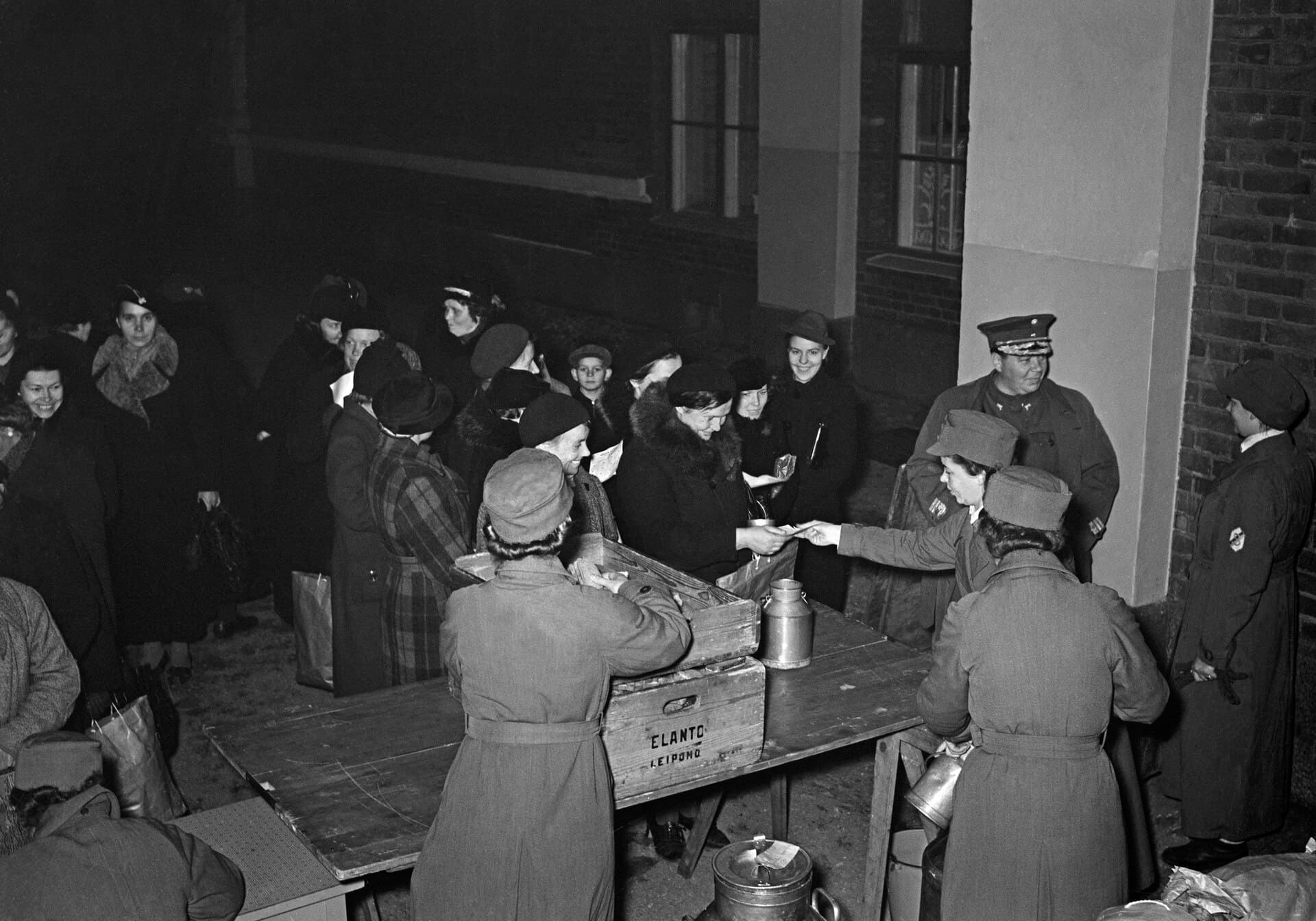 Volunteers handing out food from a long table, black and white, 1939
