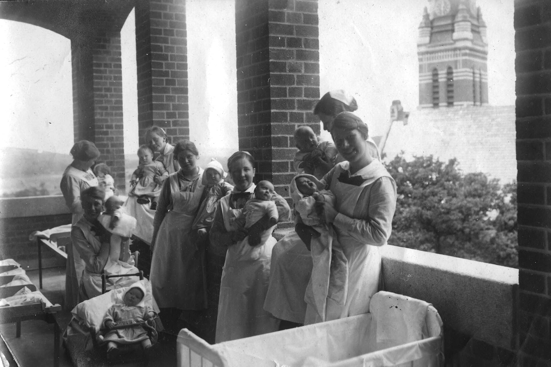 Nurses holding infants on the balcony of a hospital ward, black and white